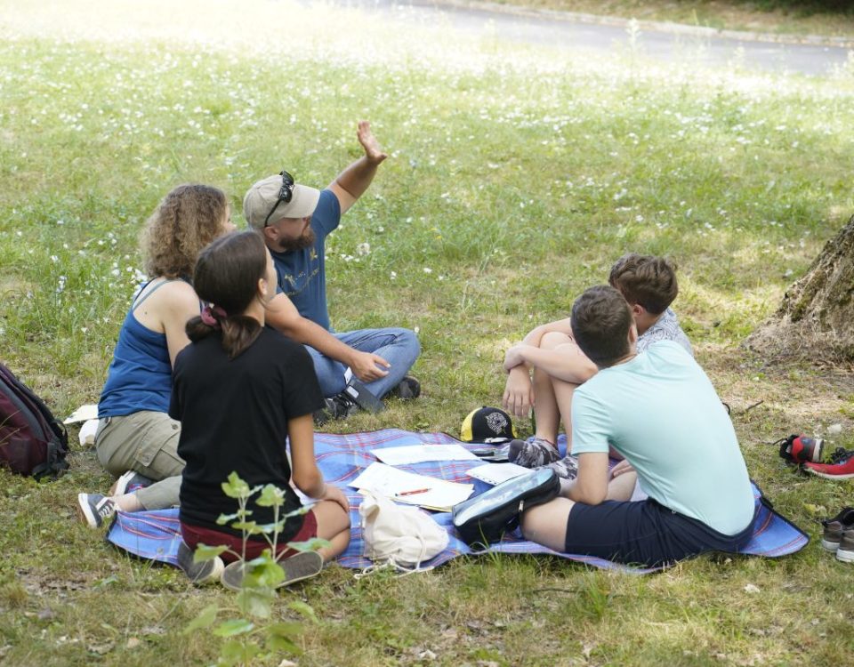 Študenti Letnej školy mladých vedcov 2023 sedia na tráve a rozprávajú sa.