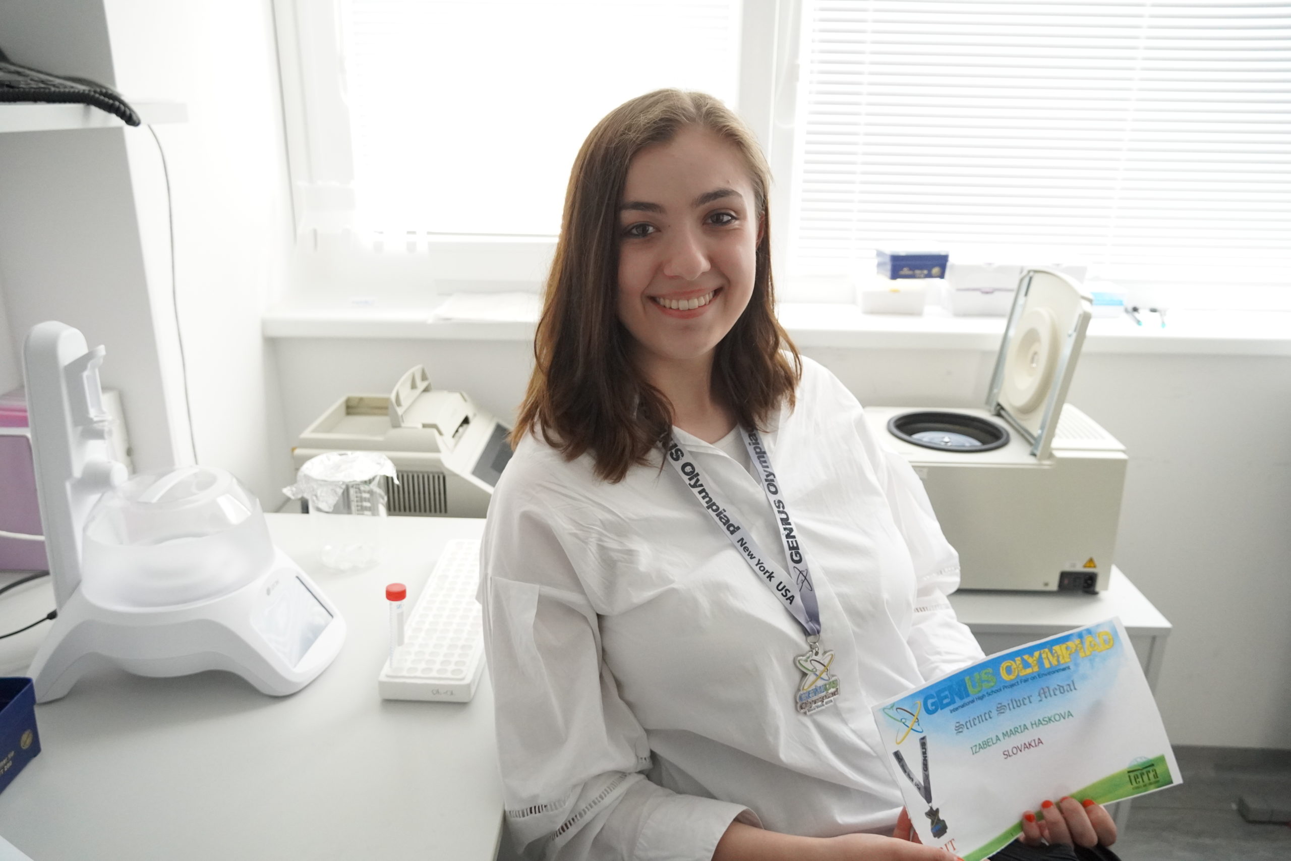 Izabela Mária Hašková, portrét v laboratóriu s diplomom a medailou zo súťaže Genius Olympiad.